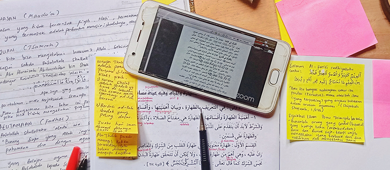 student researching an assessment on a mobile phone and taking written notes onto a pad text says when an LMS is designed for mobile first courses are accessible for more people